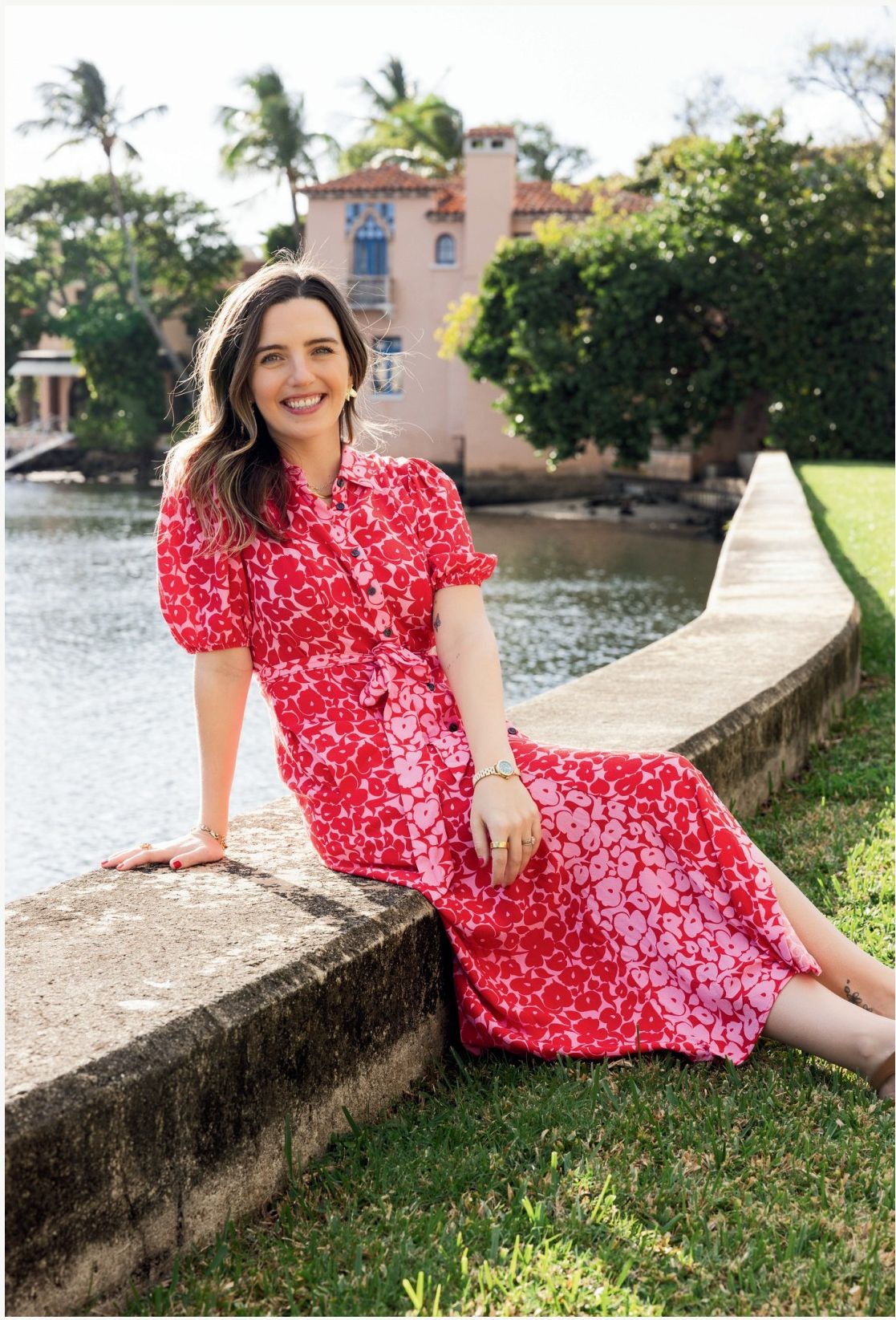 Brenna Girardi, founder, seated by the water in a red floral dress